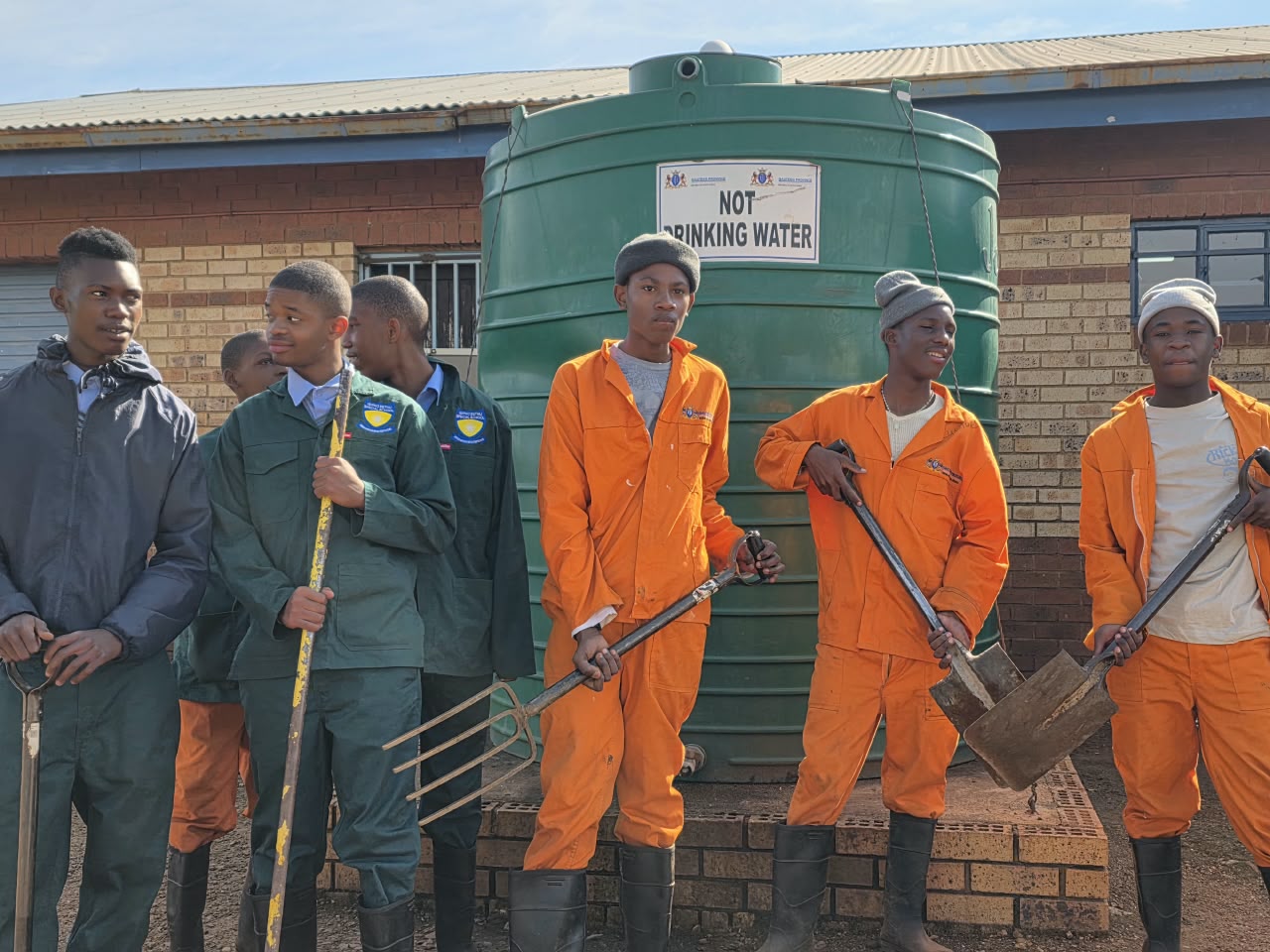Learners standing with forks and spades beside the school water tank