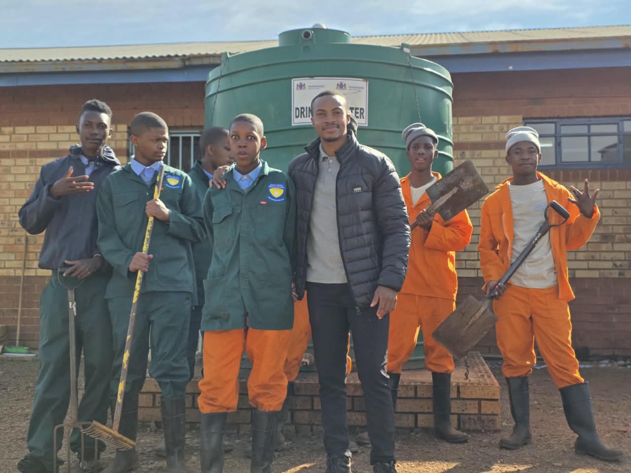 Learners and a staff member outside the school with garden tools