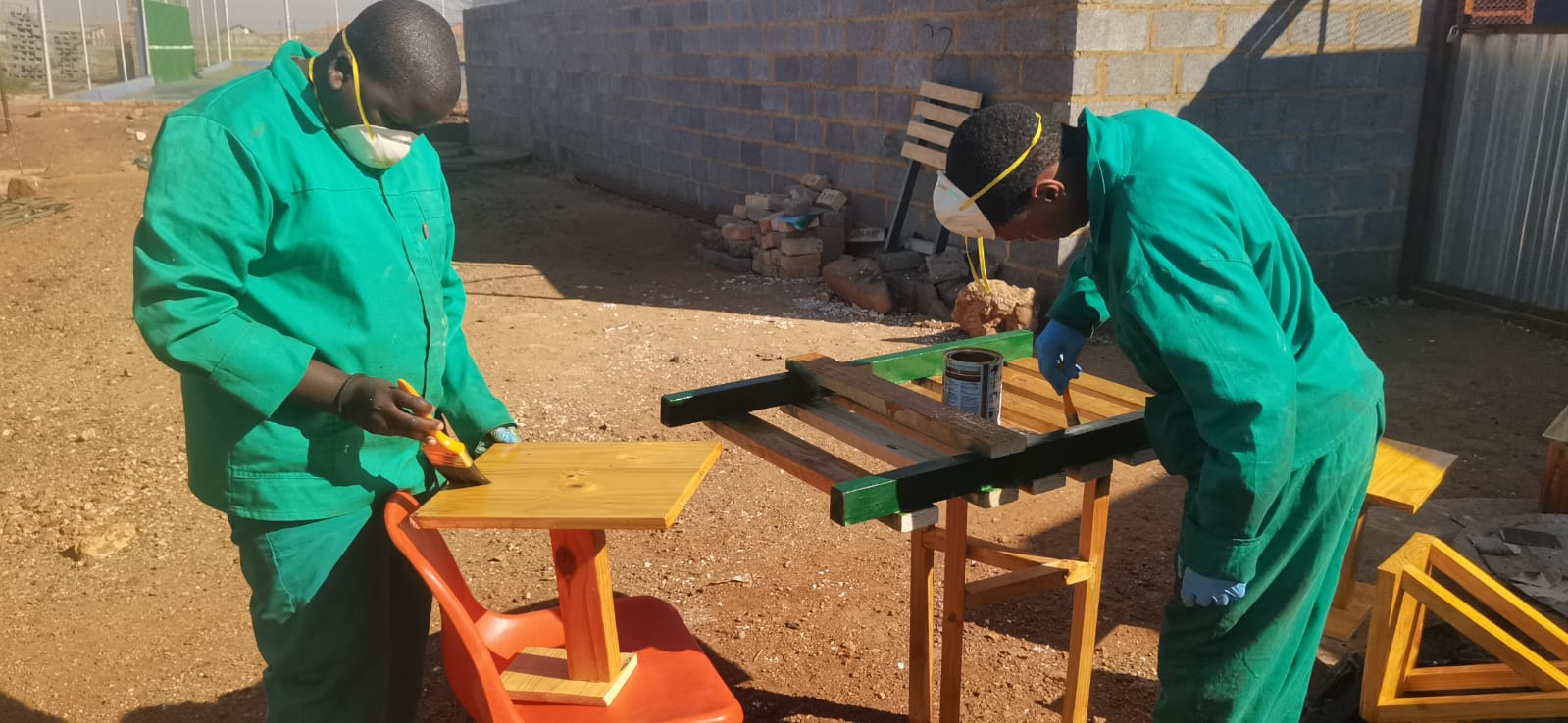 Two learners varnishing wooden tables outdoors
